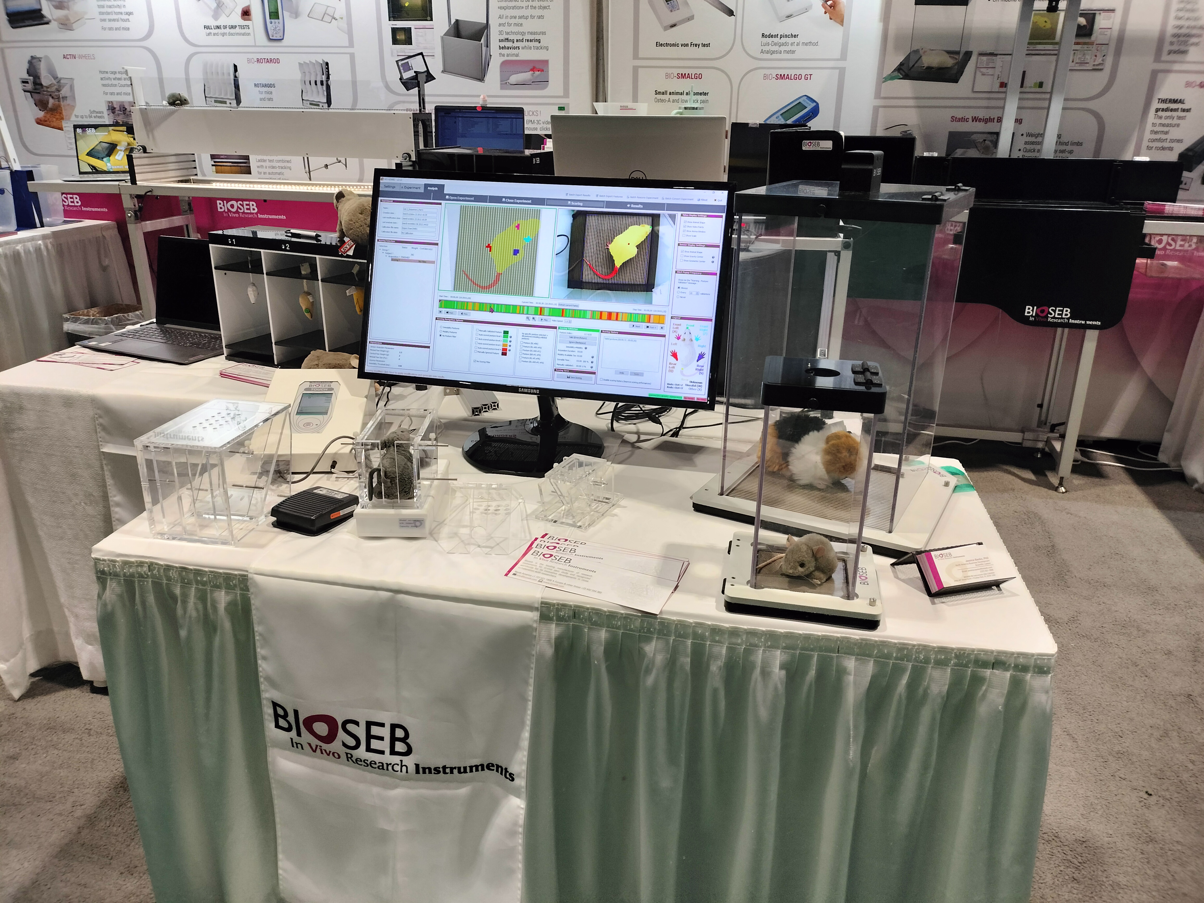 On a table, three clear specimen boxes—small, medium, and large—are arranged in front of a large computer monitor. The monitor screen displays data analysis software, which includes images of the contents of the boxes alongside a graph with vertical, multi-colored lines, similar in appearance to a spectrogram.